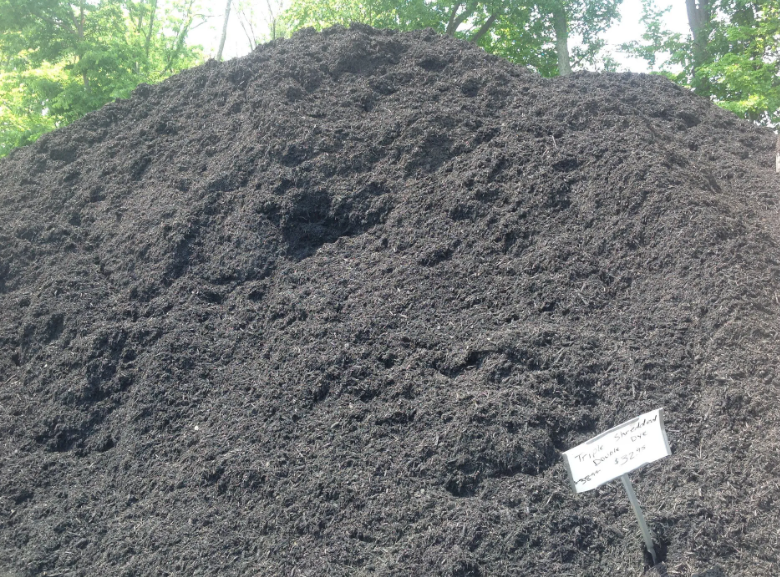 Pile of dark brown mulch outdoors, with a white sign in front.