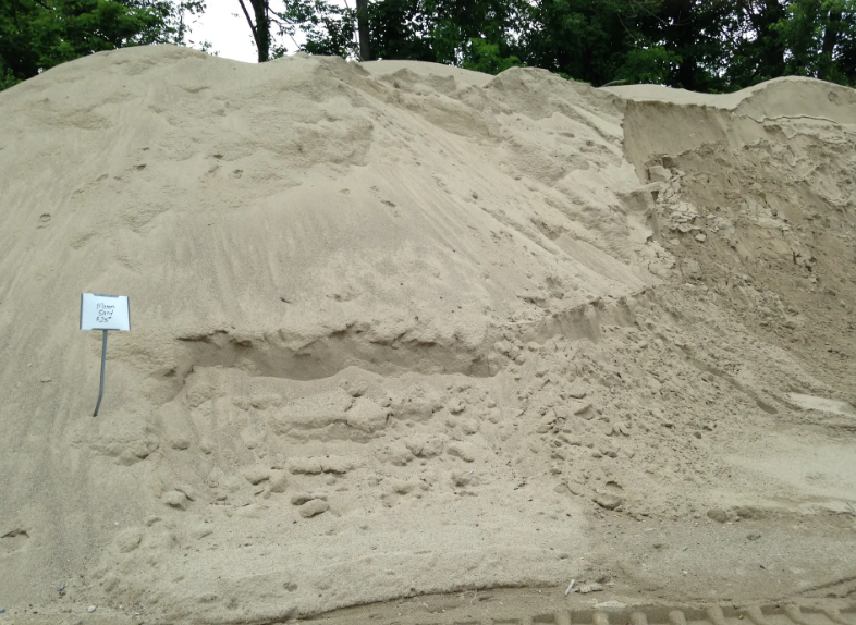 Large pile of tan sand outdoors, with a small sign at the base.