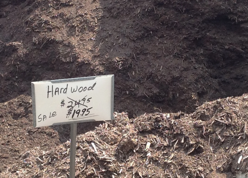 Pile of hardwood mulch; handwritten sign showing sale price of $19.95, crossed out original price $24.95.