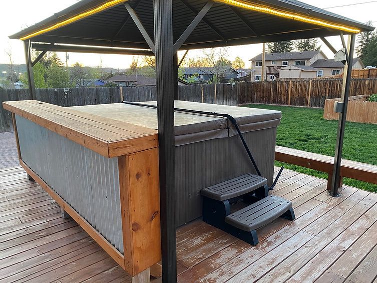 A hot tub is sitting under a gazebo on a wooden deck.