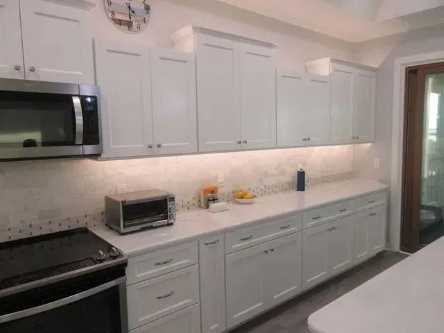 Modern white kitchen with stainless steel appliances, long counters, and light backsplash