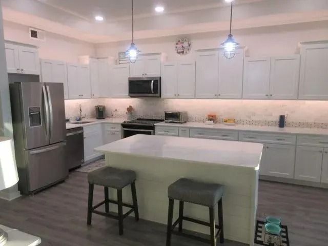 Bright modern kitchen with white cabinets, stainless fridge, island, and two stools