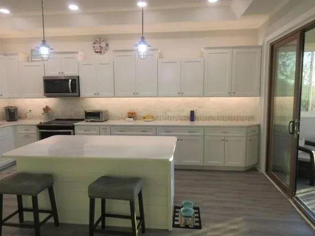 Bright kitchen with white cabinets, island, two stools, and sliding glass door.