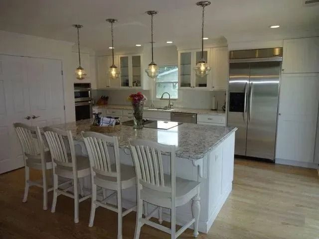 Bright kitchen with white island, four stools, stainless steel fridge, and hardwood floors