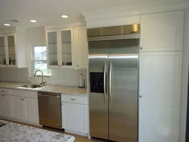Bright white kitchen with stainless steel refrigerator, dishwasher, and marble countertops