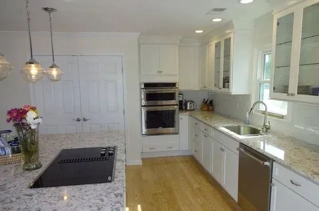 Bright modern kitchen with granite island, white cabinets, stainless appliances, and wood floor