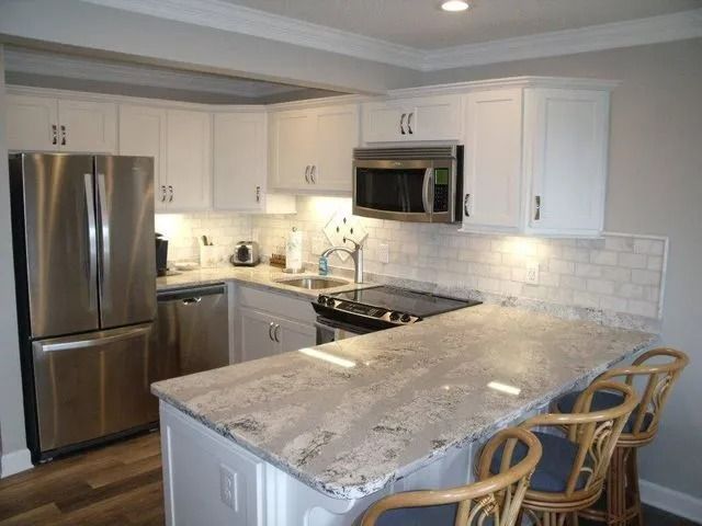 Modern kitchen with stainless steel appliances, white cabinets, and a large granite island with wicker stools