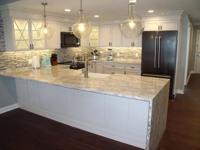 Bright modern kitchen with white cabinets, marble island, pendant lights, and dark wood floors