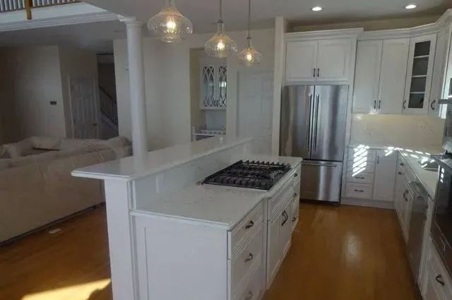 Bright white kitchen with island cooktop, stainless fridge, pendant lights, and open view to living room