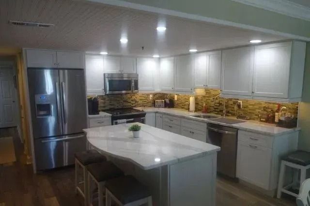 Modern white kitchen with stainless steel fridge, island, and stacks of pizza boxes on the counters