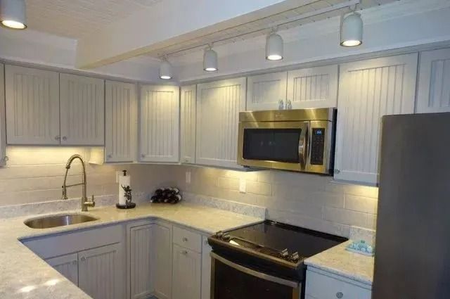 Modern white kitchen with gray cabinets, stainless appliances, and granite countertops under pendant lights