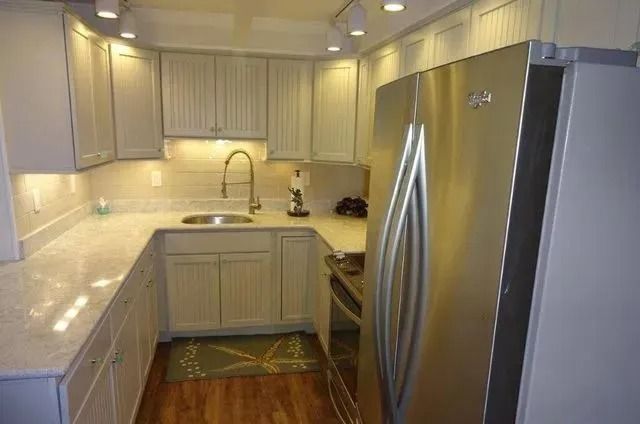 Modern kitchen with stainless steel fridge, light wood cabinets, and marble countertops