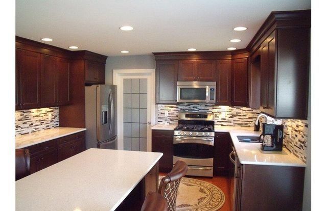 Modern kitchen with dark wood cabinets, white countertops, stainless appliances, and a large island