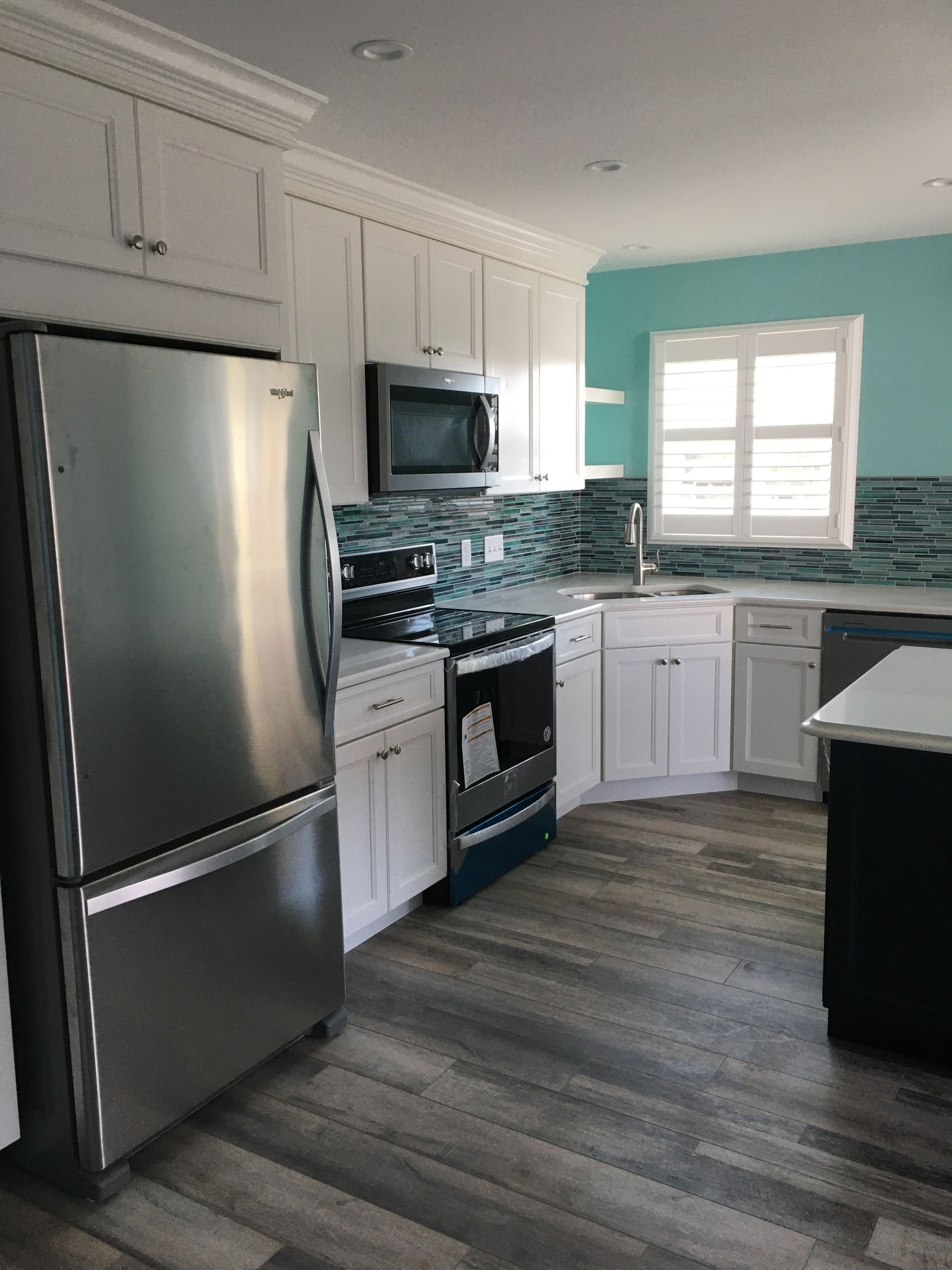 Bright modern kitchen with stainless steel appliances, white cabinets, teal accent wall, and gray wood floors