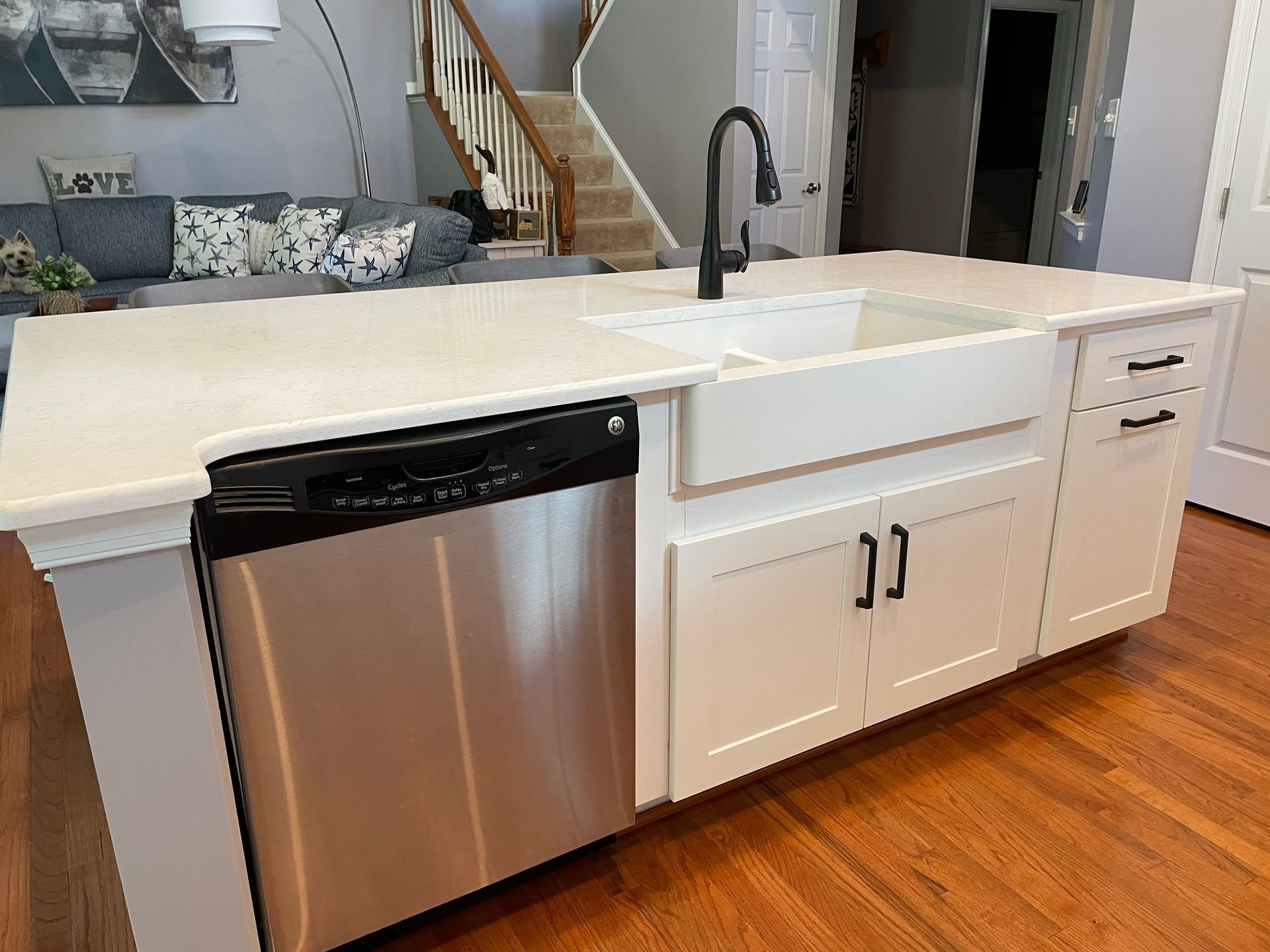 Modern kitchen with white island, stainless dishwasher, black faucet, and hardwood floor