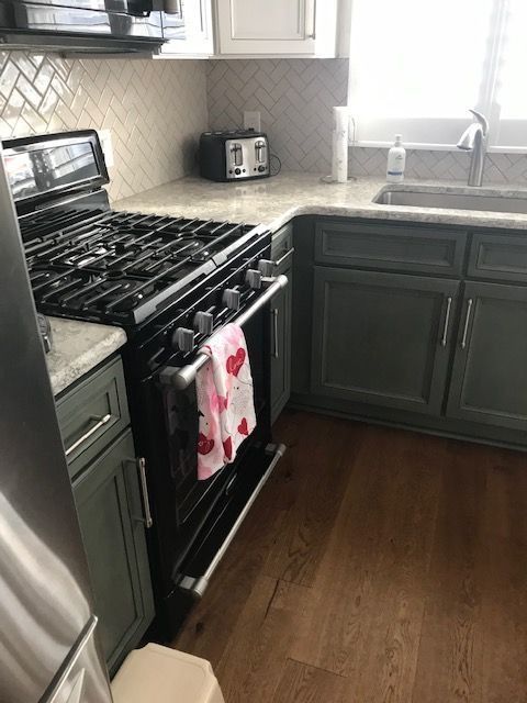 Modern kitchen with black stove, green cabinets, white countertops, and bright window by the sink