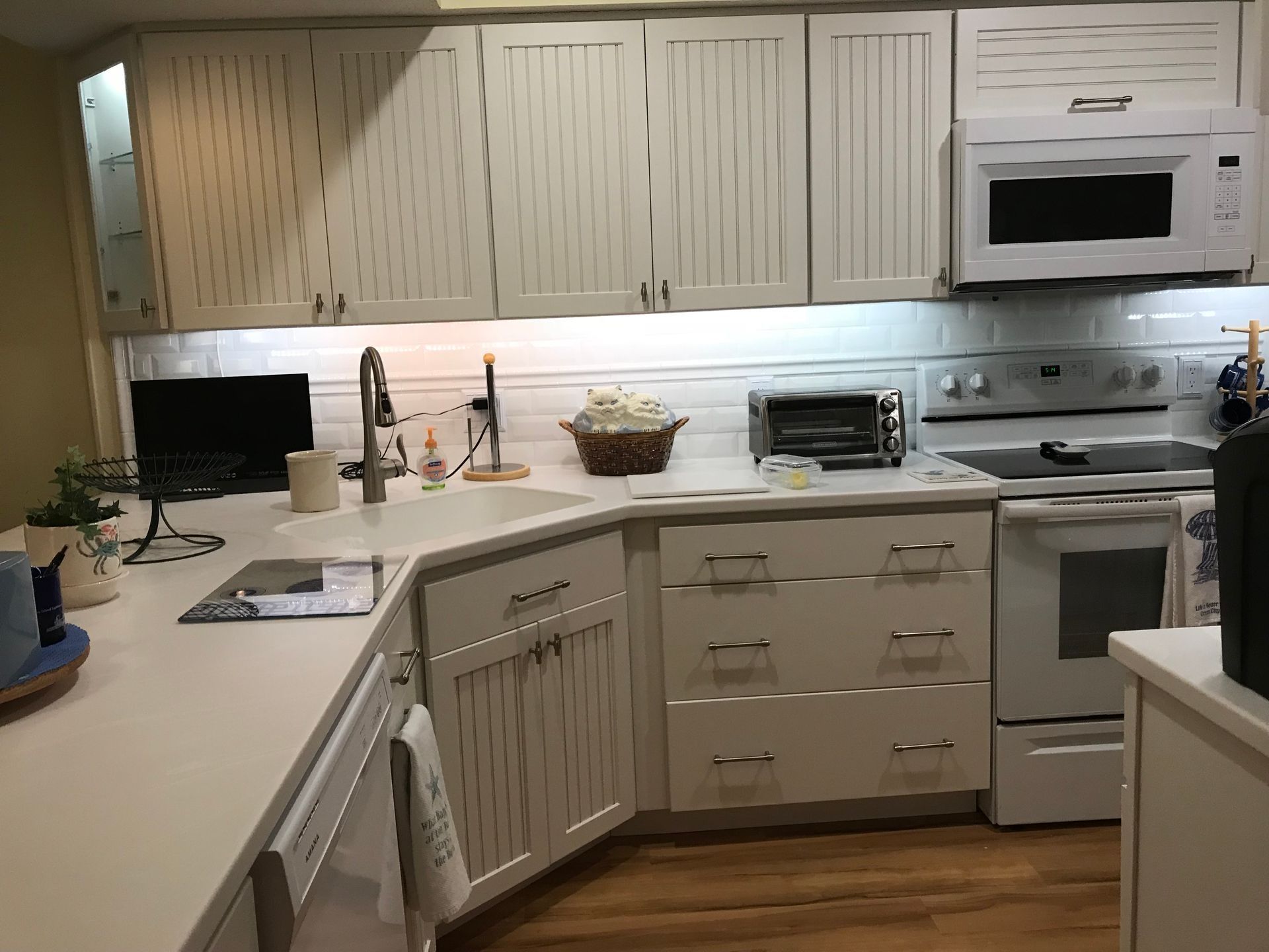 White kitchen with cabinets, countertop, sink, microwave, toaster oven, and stove.