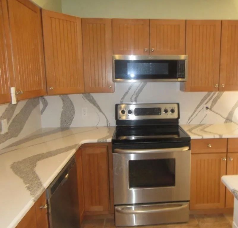 Kitchen with stainless steel stove and microwave, wood cabinets, and light granite countertops.