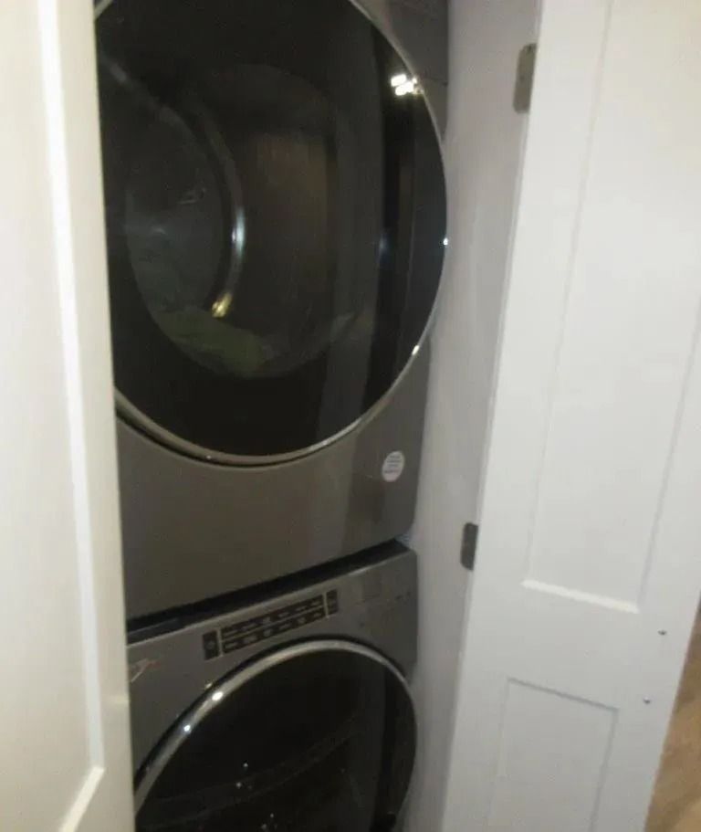 Stacked black washer and dryer in a narrow laundry closet with white doors.
