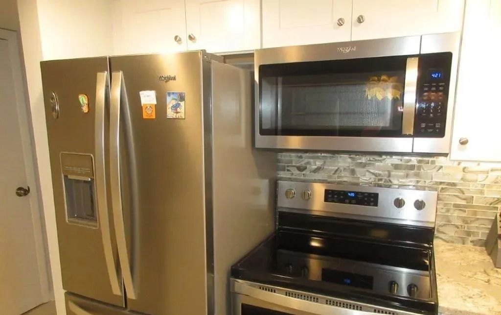 Kitchen with stainless steel refrigerator, microwave, and stove beneath light cabinets.