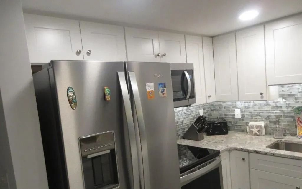 Modern kitchen with white cabinets, stainless steel refrigerator, stove, and light tiled backsplash