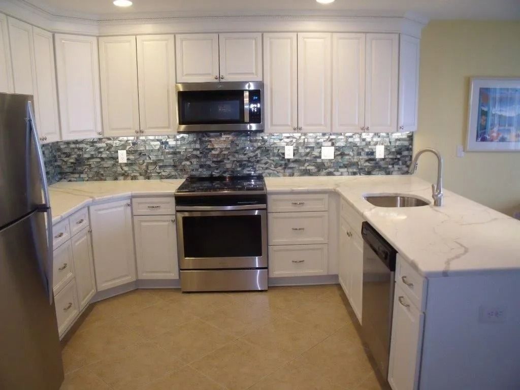 White kitchen with stainless steel appliances, white cabinets, mosaic backsplash, and granite counters
