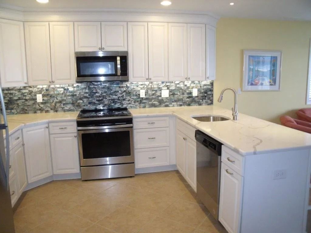 Modern white kitchen with stainless steel appliances, tiled backsplash, and light countertop peninsula
