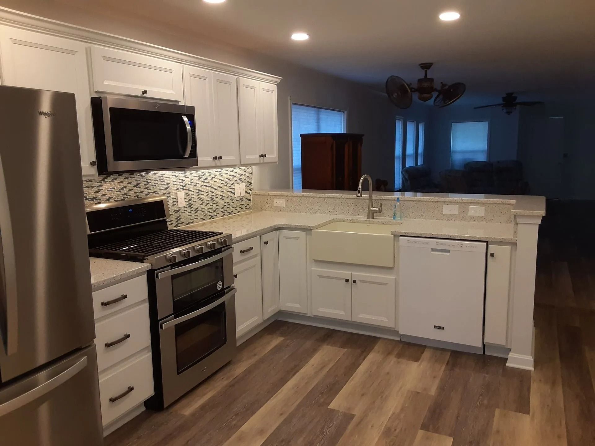 Modern kitchen with white cabinets, stainless steel appliances, and wood-look flooring under warm lighting