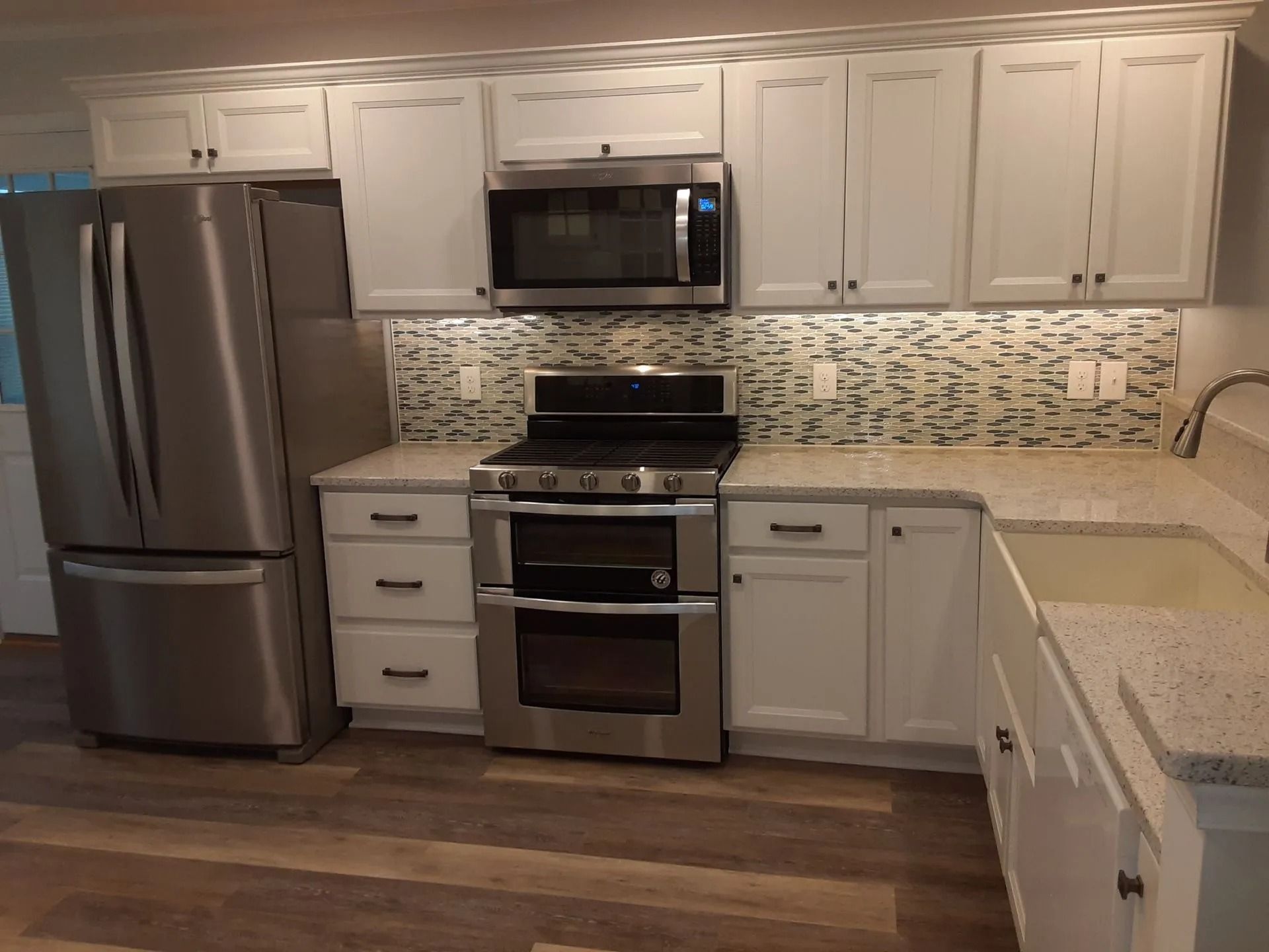 Modern kitchen with white cabinets, stainless steel appliances, mosaic backsplash, and dark wood floors