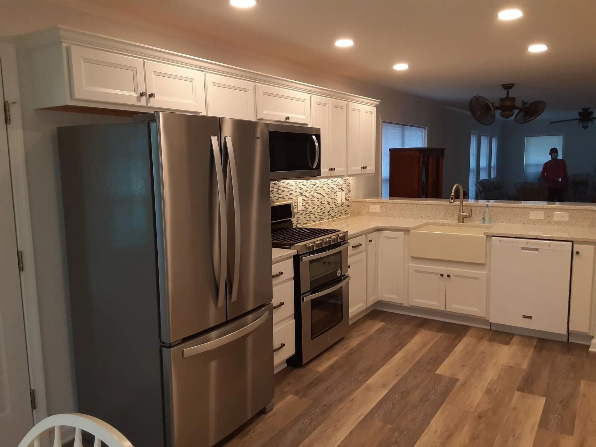 Modern kitchen with stainless steel appliances, white cabinets, wood floors, and a large island with sink