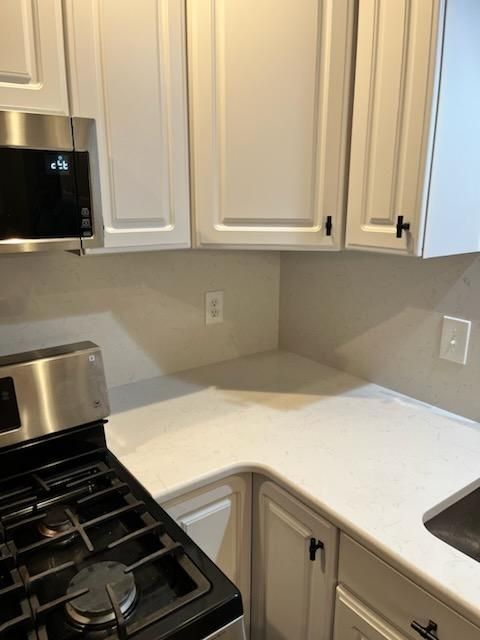 White kitchen corner with gas stove, white cabinets, and light countertop, showing outlets and a built-in microwave.