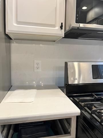 Kitchen countertop under white cabinets next to a stainless steel stove and microwave