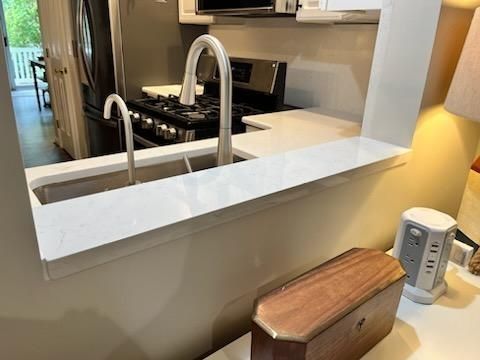 Kitchen pass-through with white counter, chrome faucet, gas stove, and small wooden cabinet on the right
