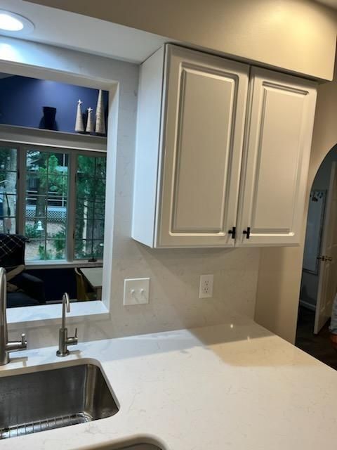 Kitchen counter with sink, white cabinets, and a window overlooking greenery.