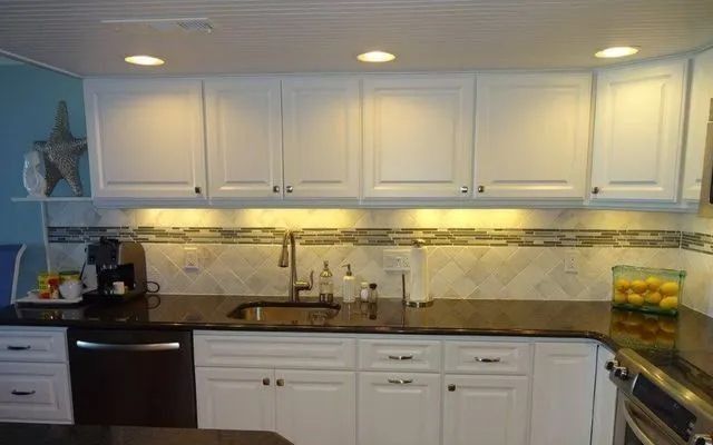 Bright kitchen with white cabinets, dark countertops, under-cabinet lighting, and fruit bowls on the counter