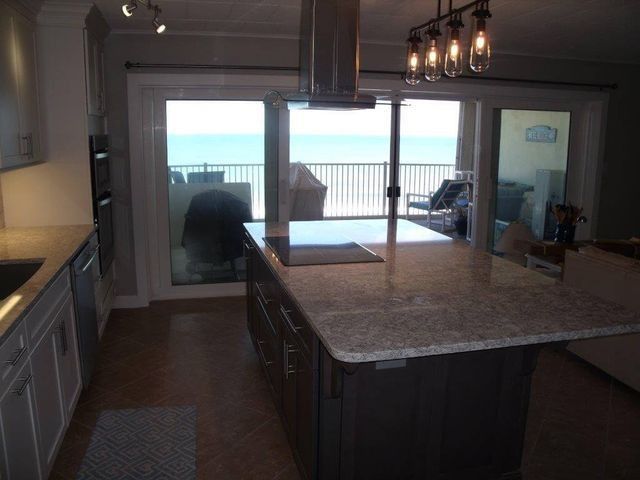Modern kitchen with granite island and pendant lights, opening to a bright patio and ocean view.