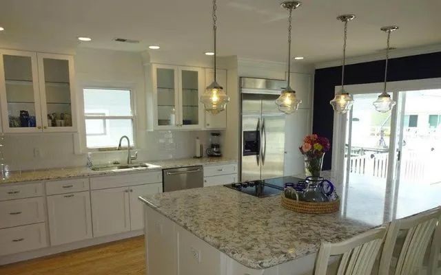 Bright white kitchen with granite island, pendant lights, and glass doors opening to a patio