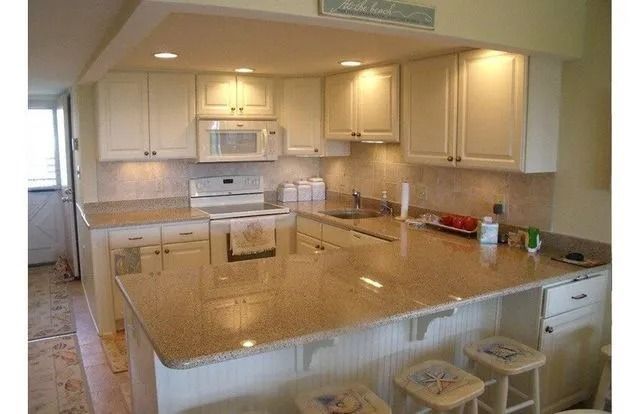 Bright kitchen with cream cabinets, granite island, stove, sink, and stools around a breakfast bar.