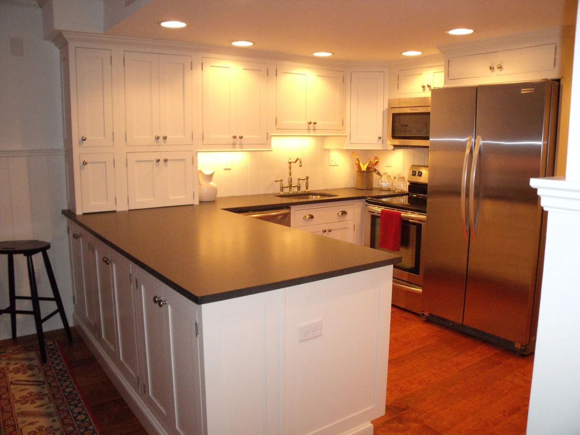 Modern white kitchen with dark countertops, stainless steel fridge, and island under warm lighting