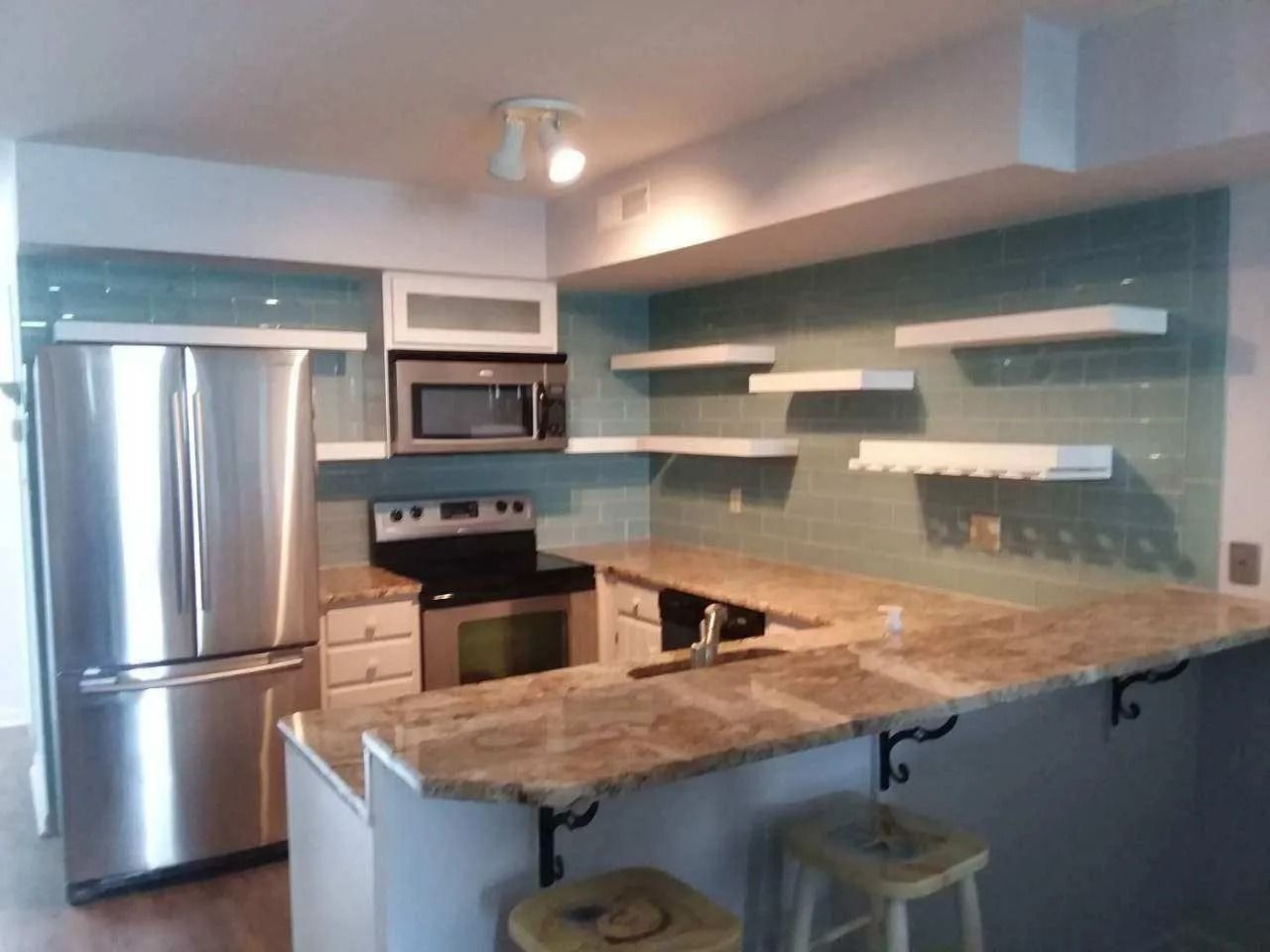 Modern kitchen with stainless steel appliances, turquoise backsplash, and a long marble island with stools