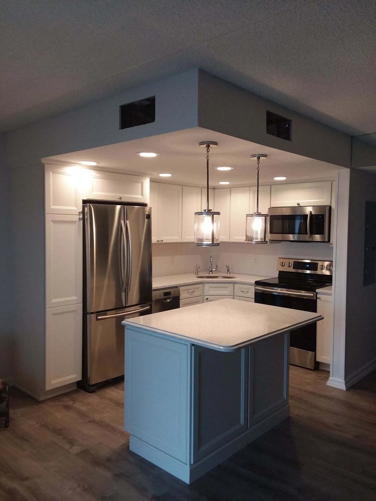 Modern white kitchen with stainless steel appliances, central island, and pendant lights