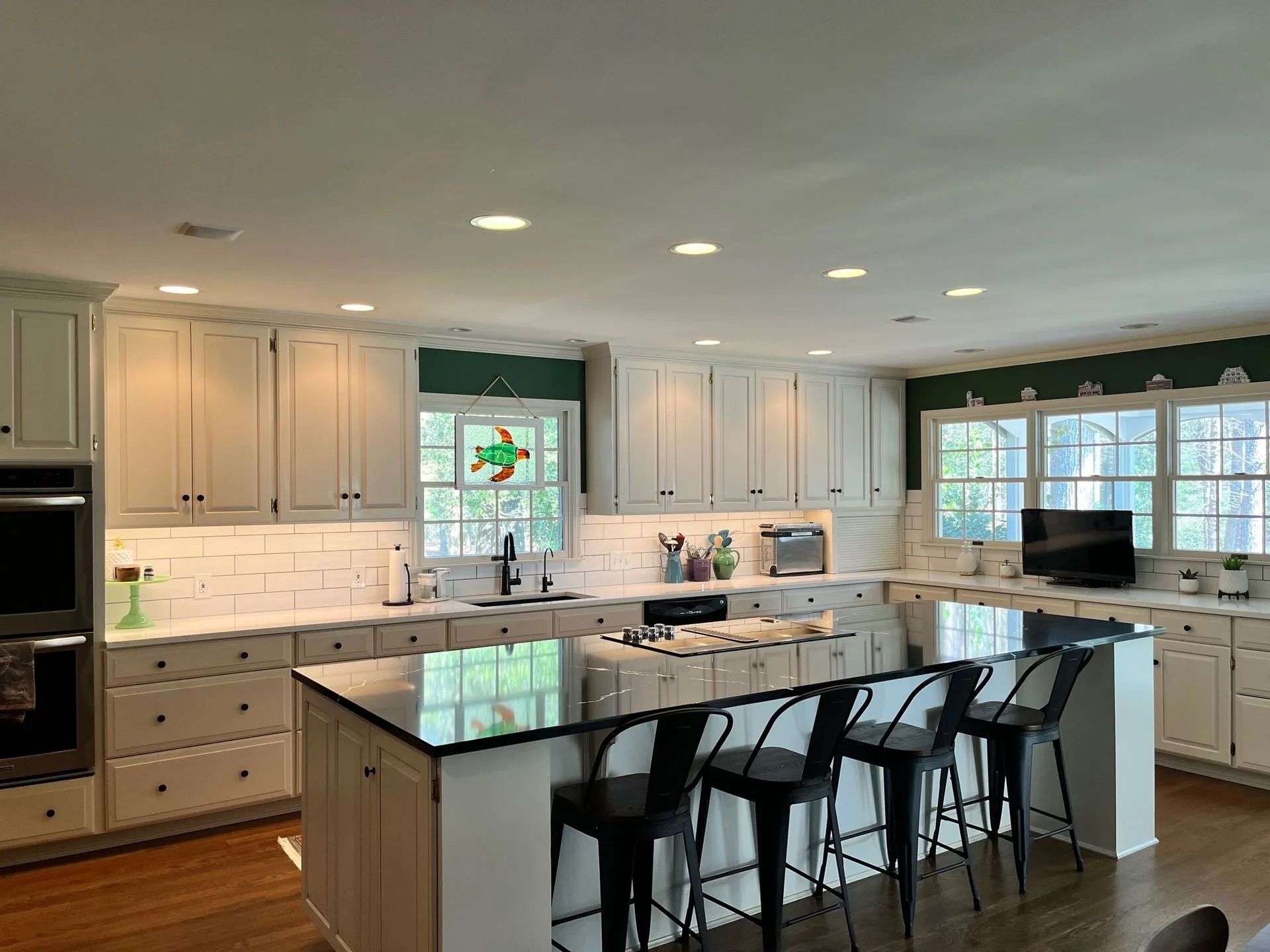 Bright modern kitchen with white cabinets, large island, and black bar stools underneath pendant lights.