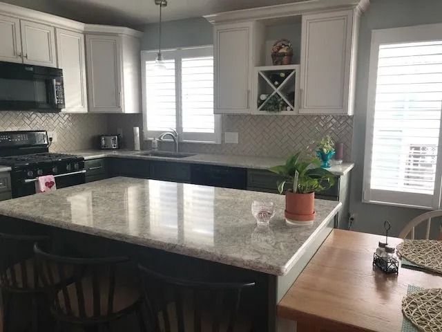 Bright kitchen with white cabinets, dark island, and potted plants by the sink and window.