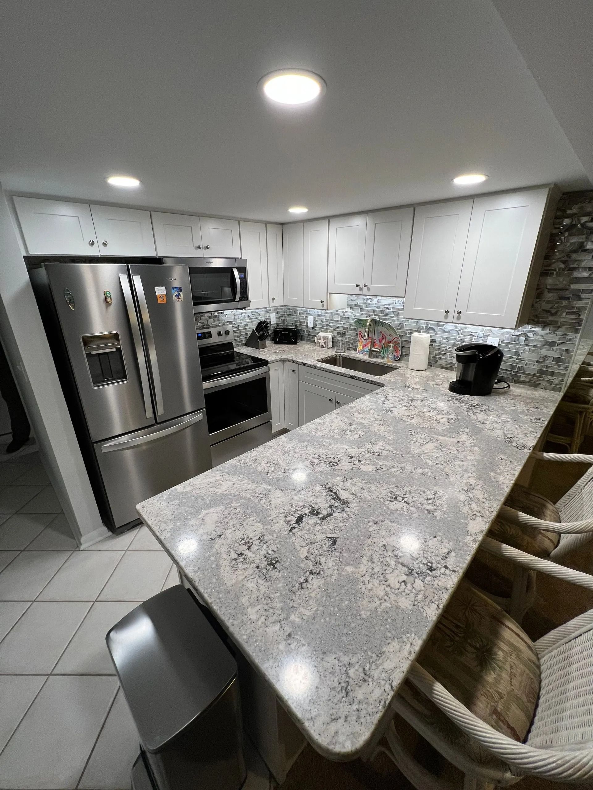 Modern kitchen with granite island, stainless steel appliances, and bar stools under bright ceiling light