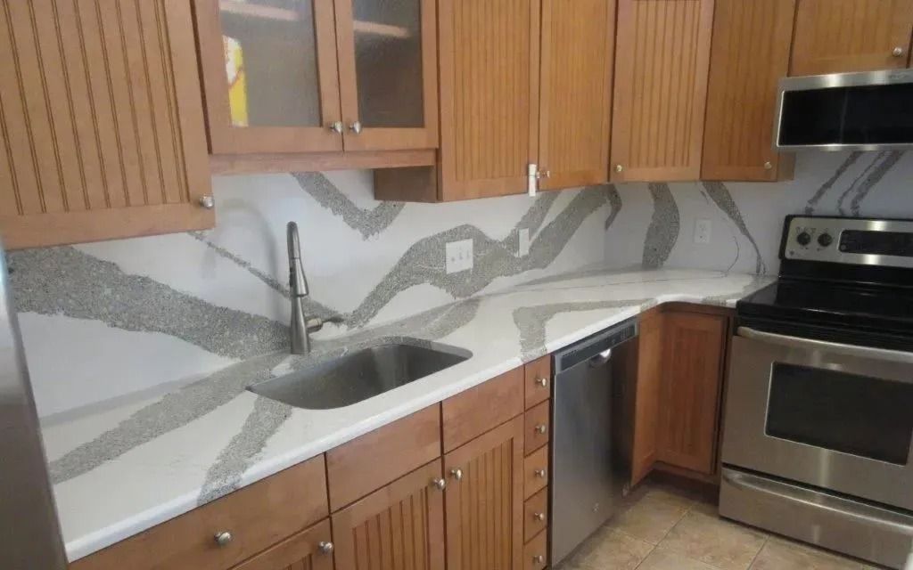 Modern kitchen with wood cabinets, stainless steel appliances, and a sink under gray wave-pattern backsplash.