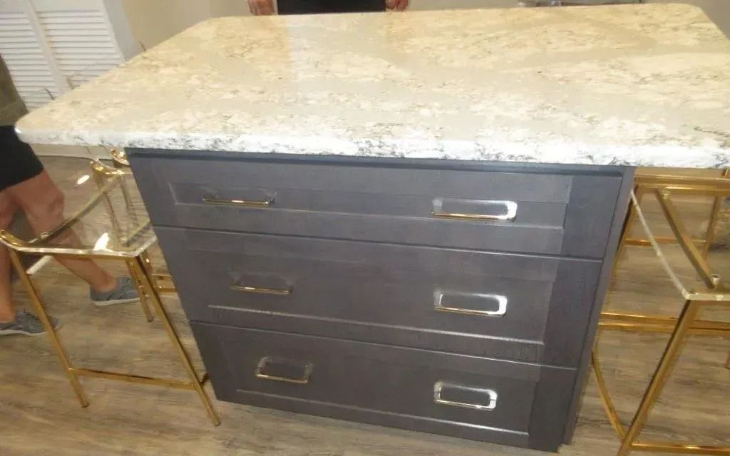 Dark wood vanity with white marble top and three drawers, flanked by gold chairs.