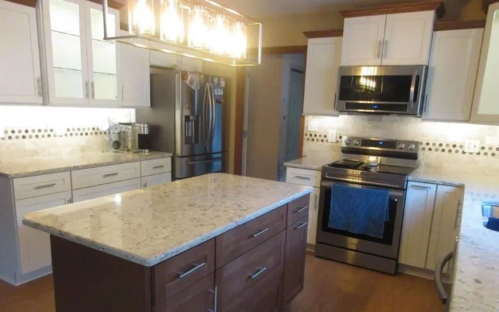 Modern kitchen with granite island, stainless steel appliances, white cabinets, and pendant lights