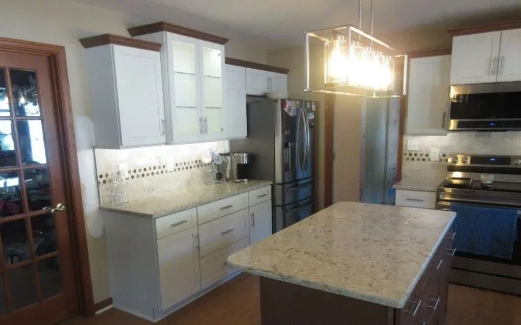 Modern kitchen with white cabinets, granite island, stainless steel appliances, and a glass pendant light.