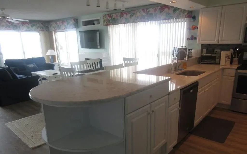 Bright kitchen with white cabinets, island, and sunlit dining area with large windows.