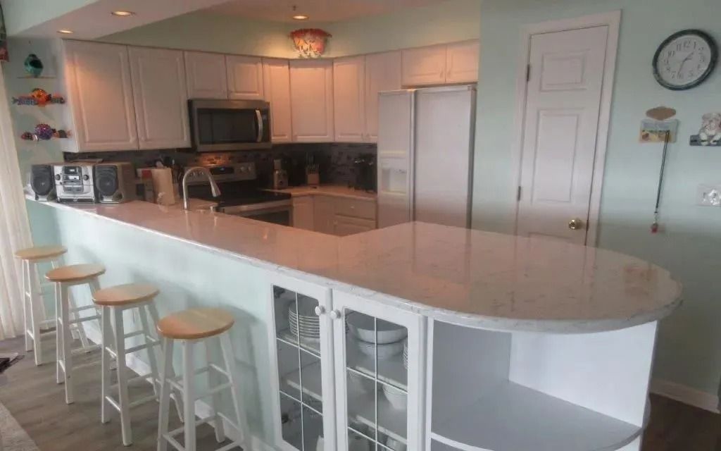 Bright kitchen with white island, bar stools, and light cabinets in a home interior.